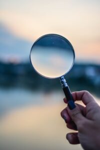 A hand is holding a magnifying glass against a blurry background.