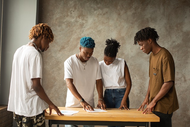 Four African-Americans standing around a table looking intently at papers on a wood table.