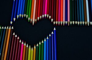 A variety of colored pencils create a heart shape on a black background.