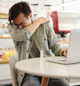 Man working on laptop sneezes into his elbow.