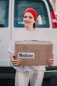 Smiling woman wearing a red bandana on her head is carrying a box marked "medicine."