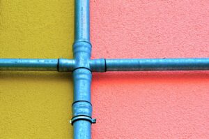 Joined pipes painted turquoise against a yellow and pink cement background