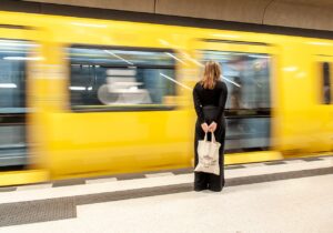 Woman holding bag standing in front of blurry yellow train on platform.