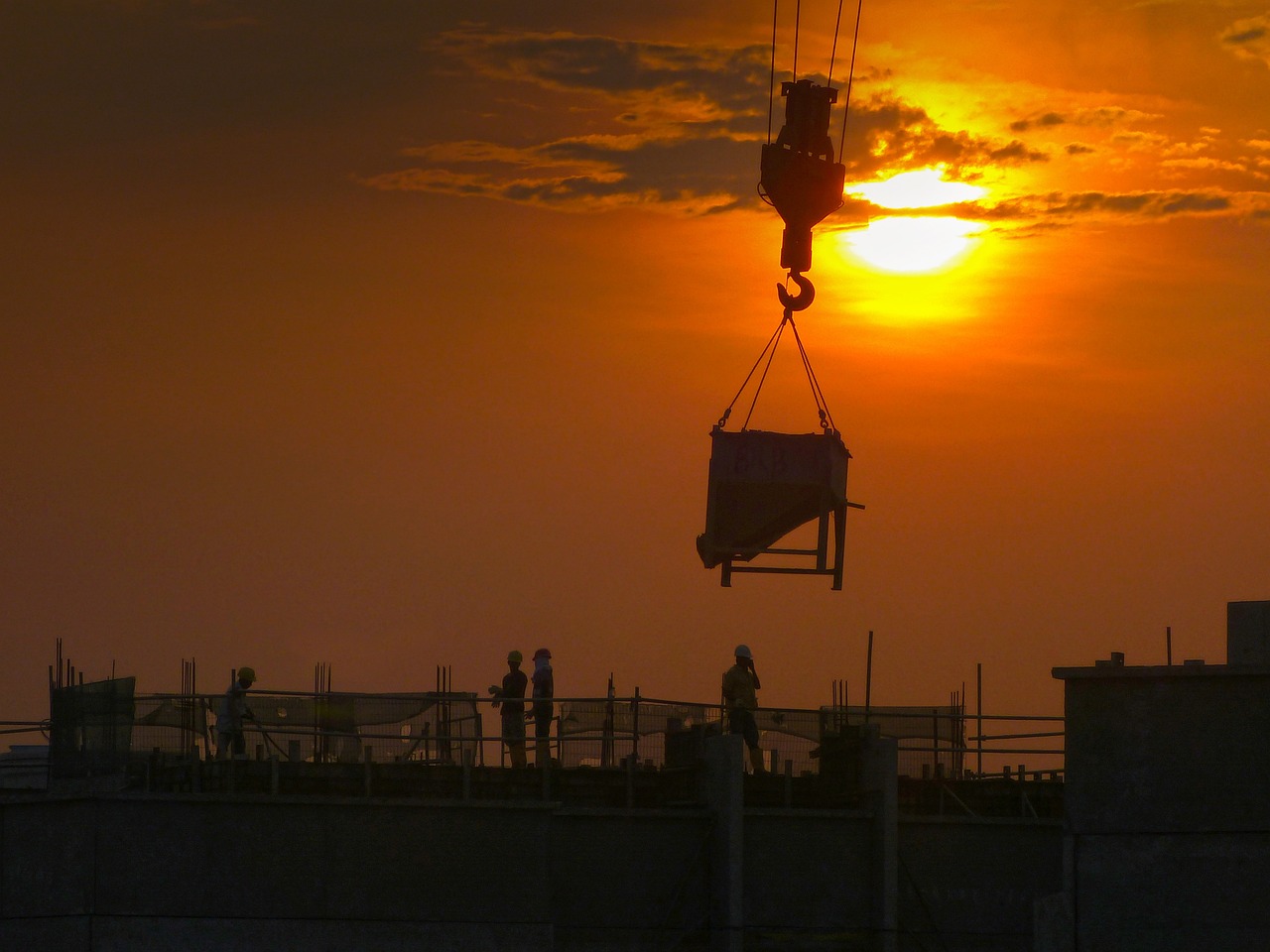Construction crane and workers on top of in-progress building with sunset in the background