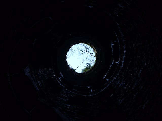 View of a deep well from the bottom looking up to see the sky through the hole at the top.