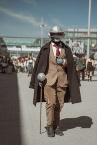 Robot dressed in brown suite and cape, walking with a walking stick.