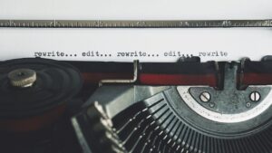 Old-fashioned manual typewriter wheel and ribbon, paper in typewriter reads, "rewrite...edit...rewrite...edit...rewrite."