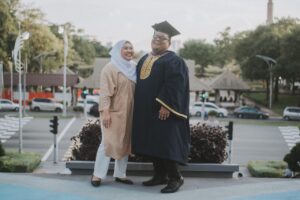 Smiling man in graduation cap and gown standing next to smiling woman.