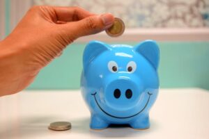 Person adding money to a smiling blue piggy bank.