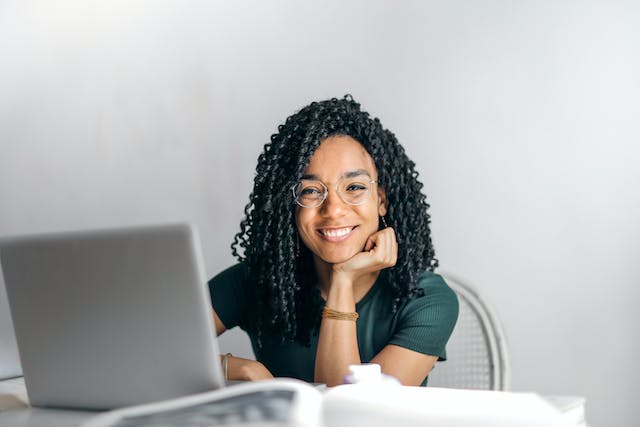 Young smiling woman with long dark curly hair sitting at laptop.