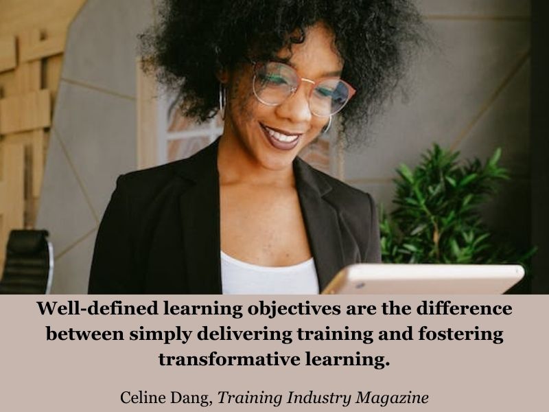 Smiling woman wearing white blouse and black blazer looking at tablet device. Quote: “Well-defined learning objectives are the difference between simply delivering training and fostering transformative learning.” Quote by Celine Dang from Training Industry Magazine.