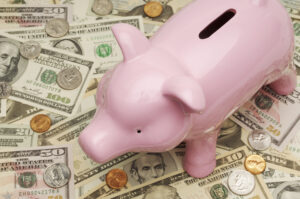 Pink piggy back on top of pile of cash and coins.