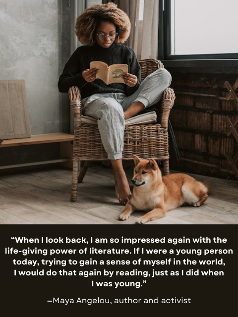 Young dark-skinned person sitting in chair reading a book, with a dog at their feet.