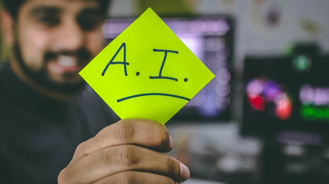 Smiling person holding up lime green sticky note with "A.I." written on it in navy marker.