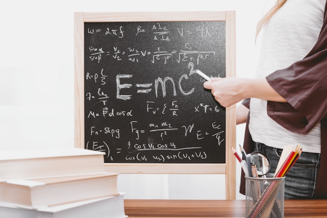 Person standing next to small blackboard that is full of equations.