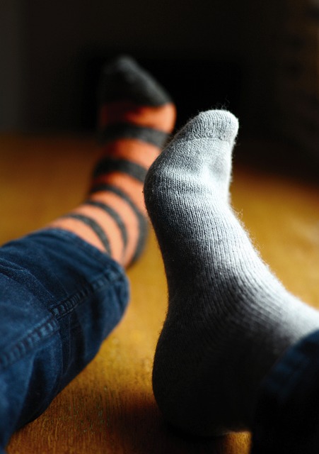 Person wearing a solid light grey sock on one foot and a black and orange striped sock on the other foot.