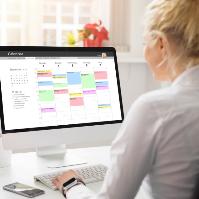 Smiling person looking at color-coded calendar on monitor.