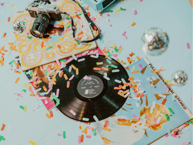 Vinyl record, several album covers, a camera, and a few silver sparkly balls are on a light blue background.