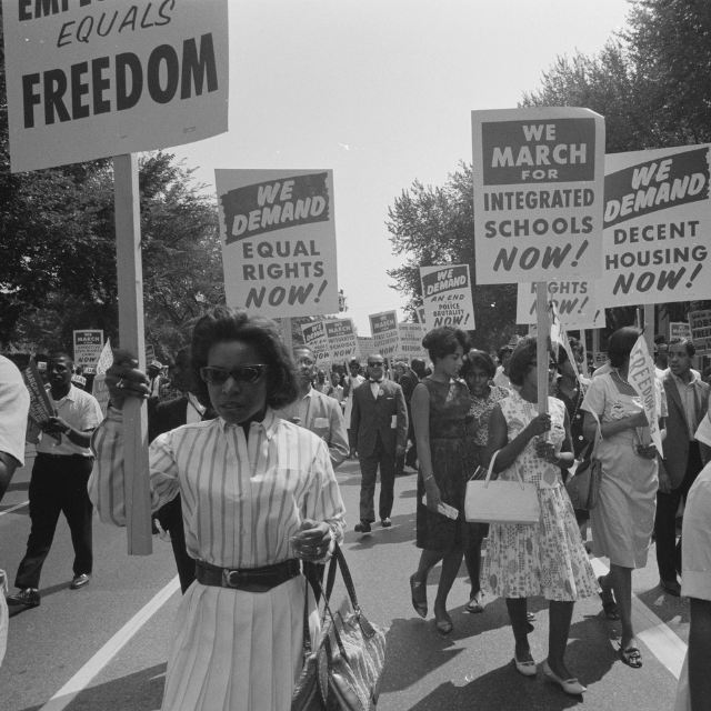 Black and white photo of civil rights protestors carrying signs about housing, freedom, and integration.