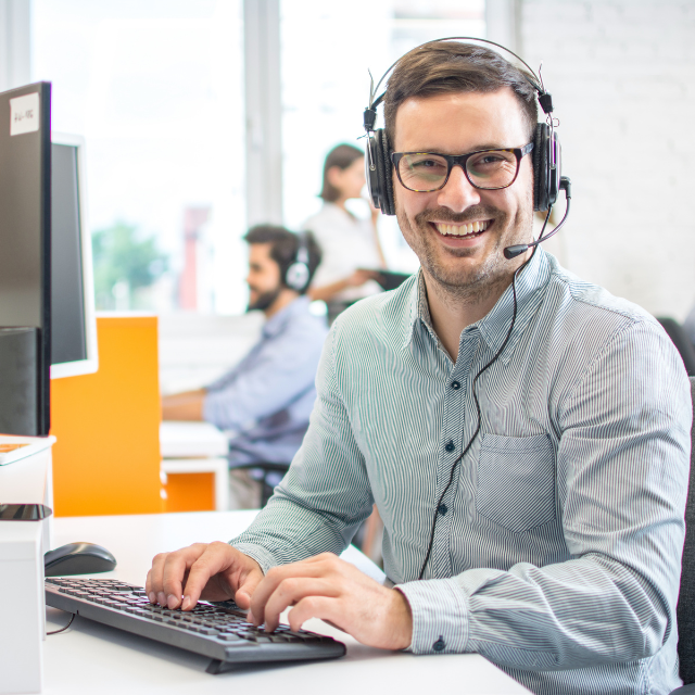 Smiling person wearing headset working at a computer.