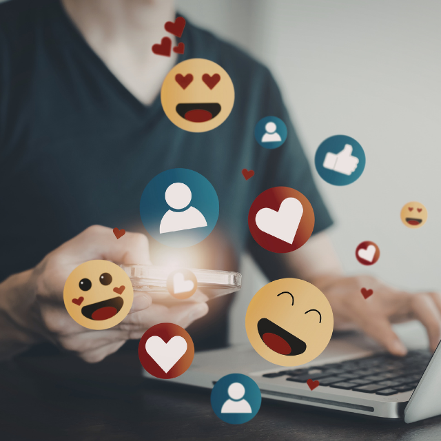 Person using laptop and mobile phone. Emojis are coming out of the screens.