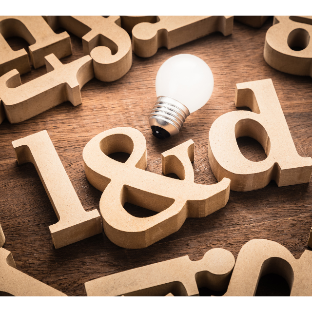 Wooden letter blocks spelling "L&D" with a light bulb resting among scattered letters, symbolizing learning, innovation, and workplace development.